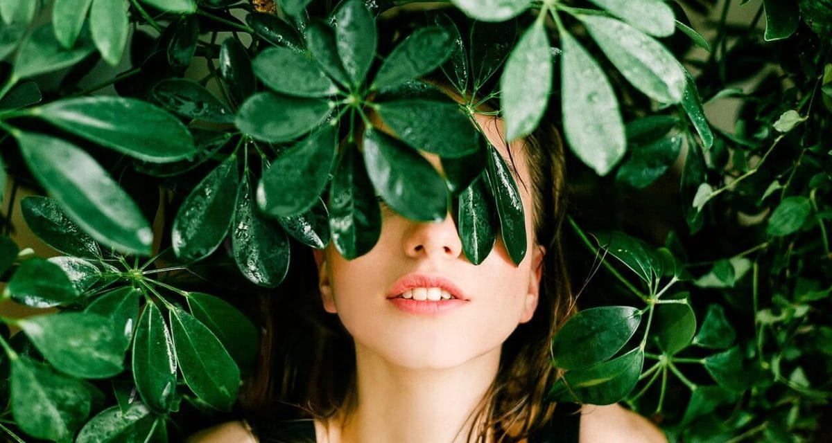 A woman concealed amidst forest foliage, peering out from behind a curtain of leaves.