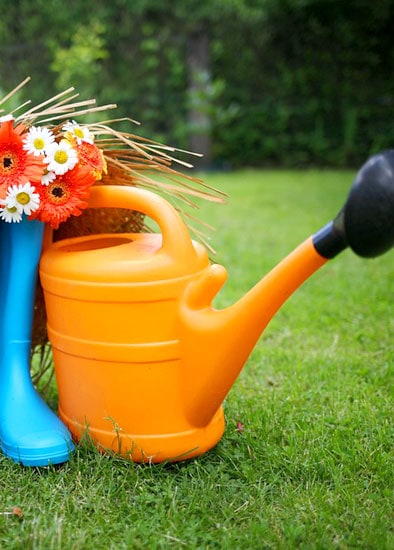 Watering can, boots, and flower basket on grass in a garden.